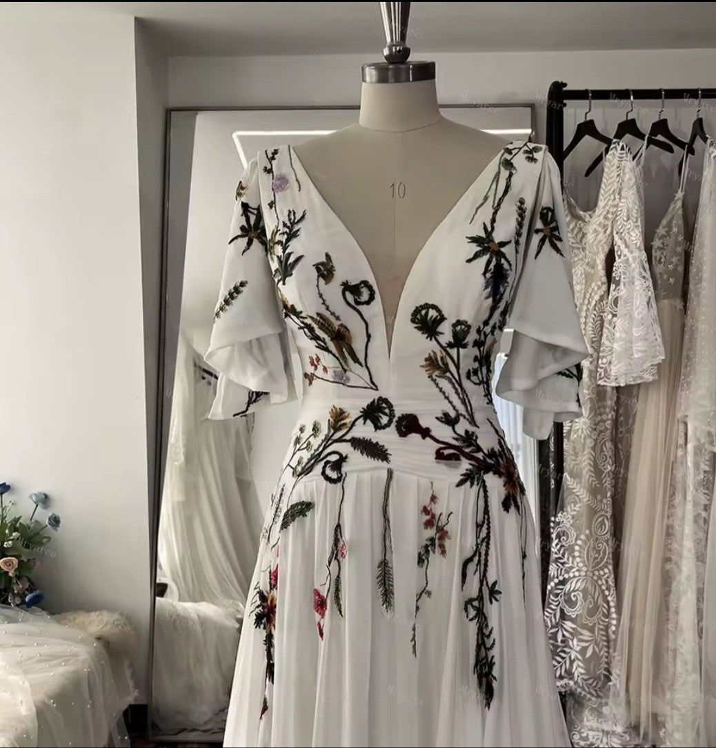 White dress with floral embroidery on a mannequin in a room with other dresses.