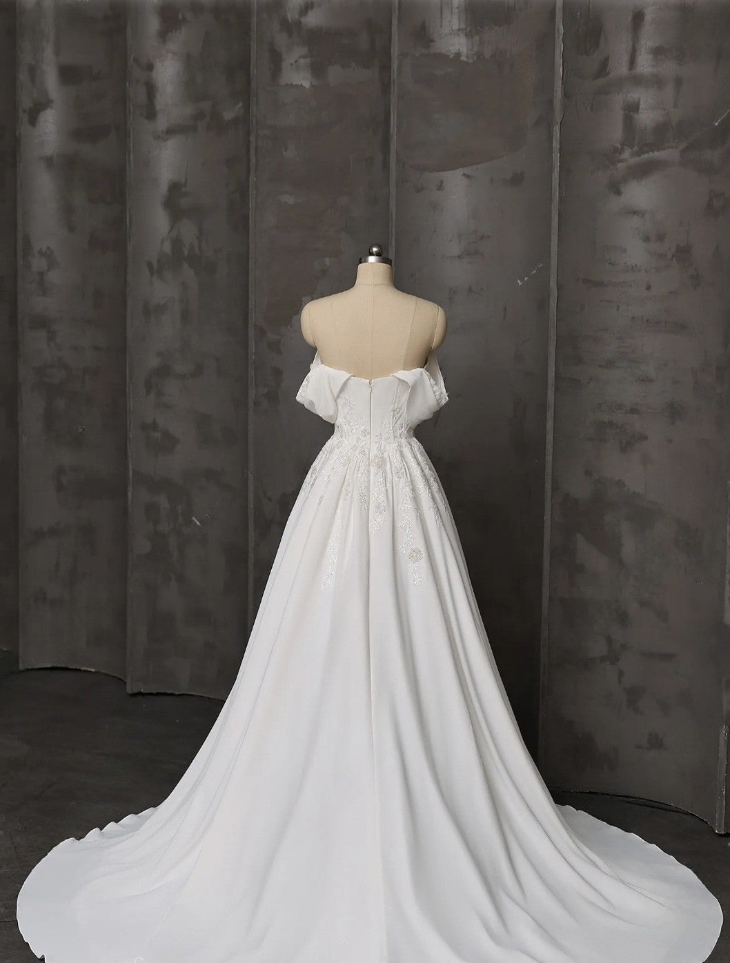 White off-shoulder wedding dress on a mannequin against a dark curtain background