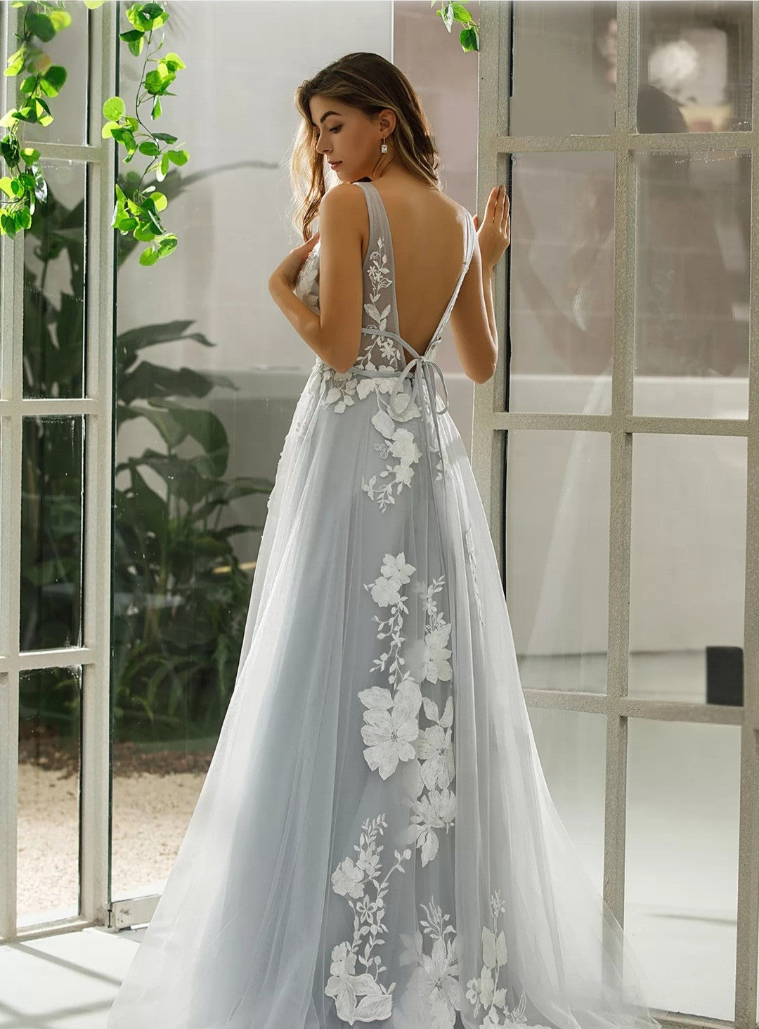 Woman in a light blue dress with floral lace details standing in a bright room.