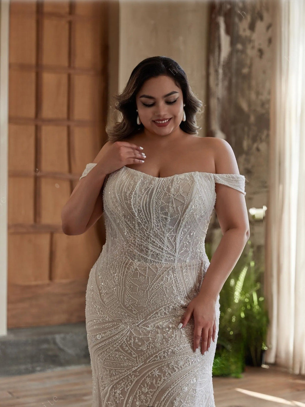 Woman wearing a white off-shoulder dress with intricate patterns, standing indoors.