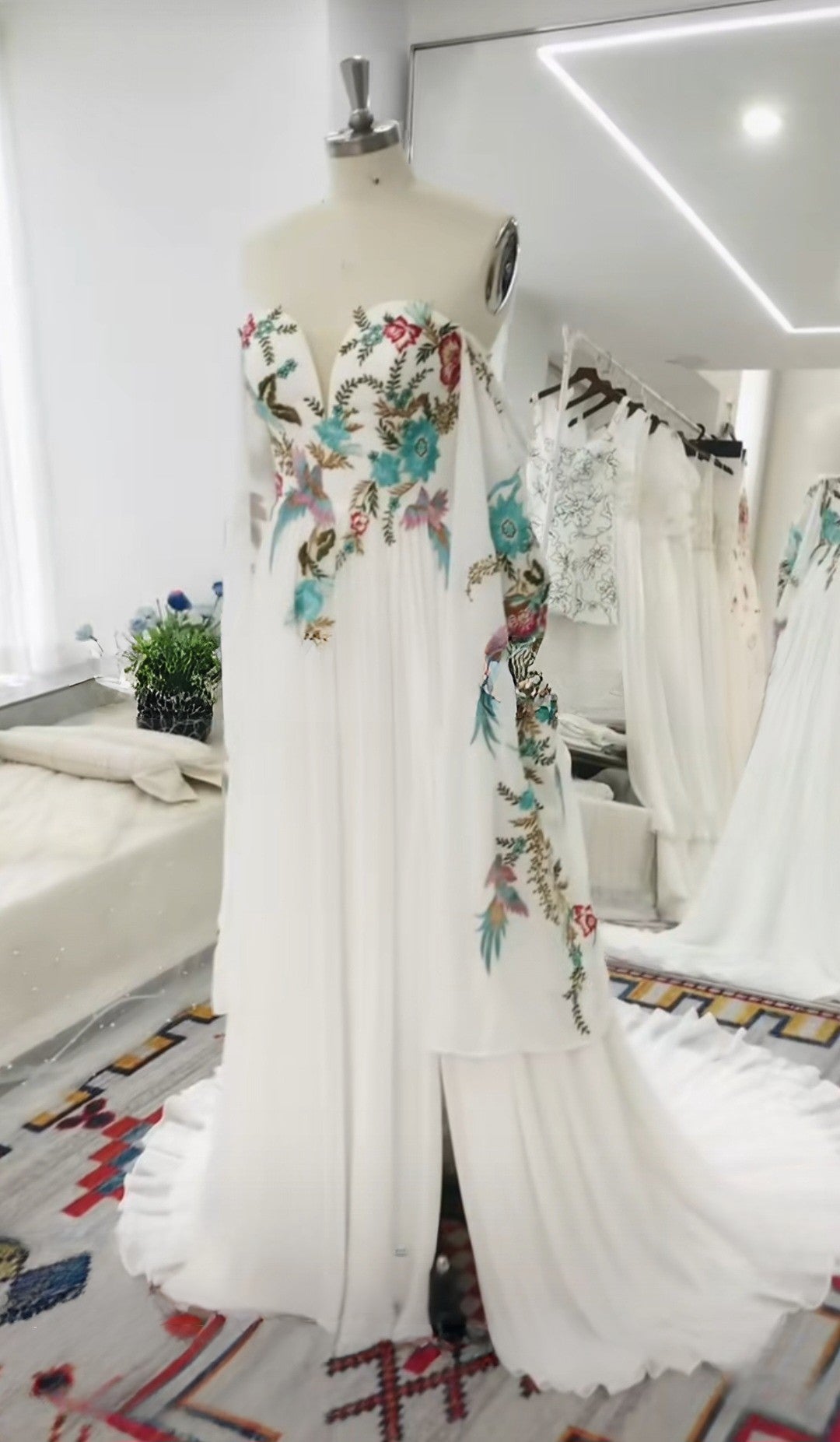 Mannequin wearing a white dress with colorful floral embroidery in a room setting.