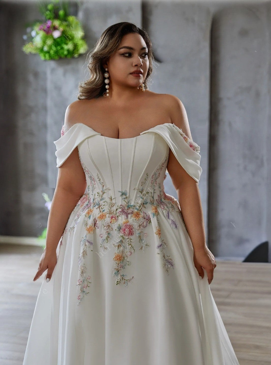 Woman wearing a white off-shoulder wedding dress with floral embroidery in an indoor setting.