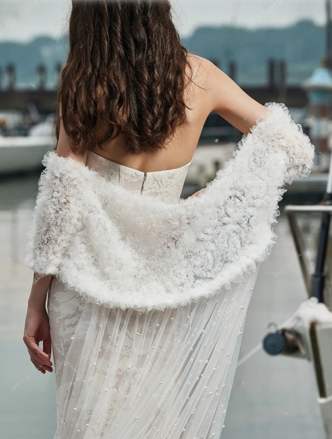 Woman wearing a white off-shoulder dress with a textured shawl in an outdoor setting.