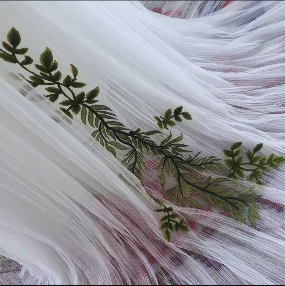 Close-up of embroidered fabric with green leaves and pink flowers on a white background