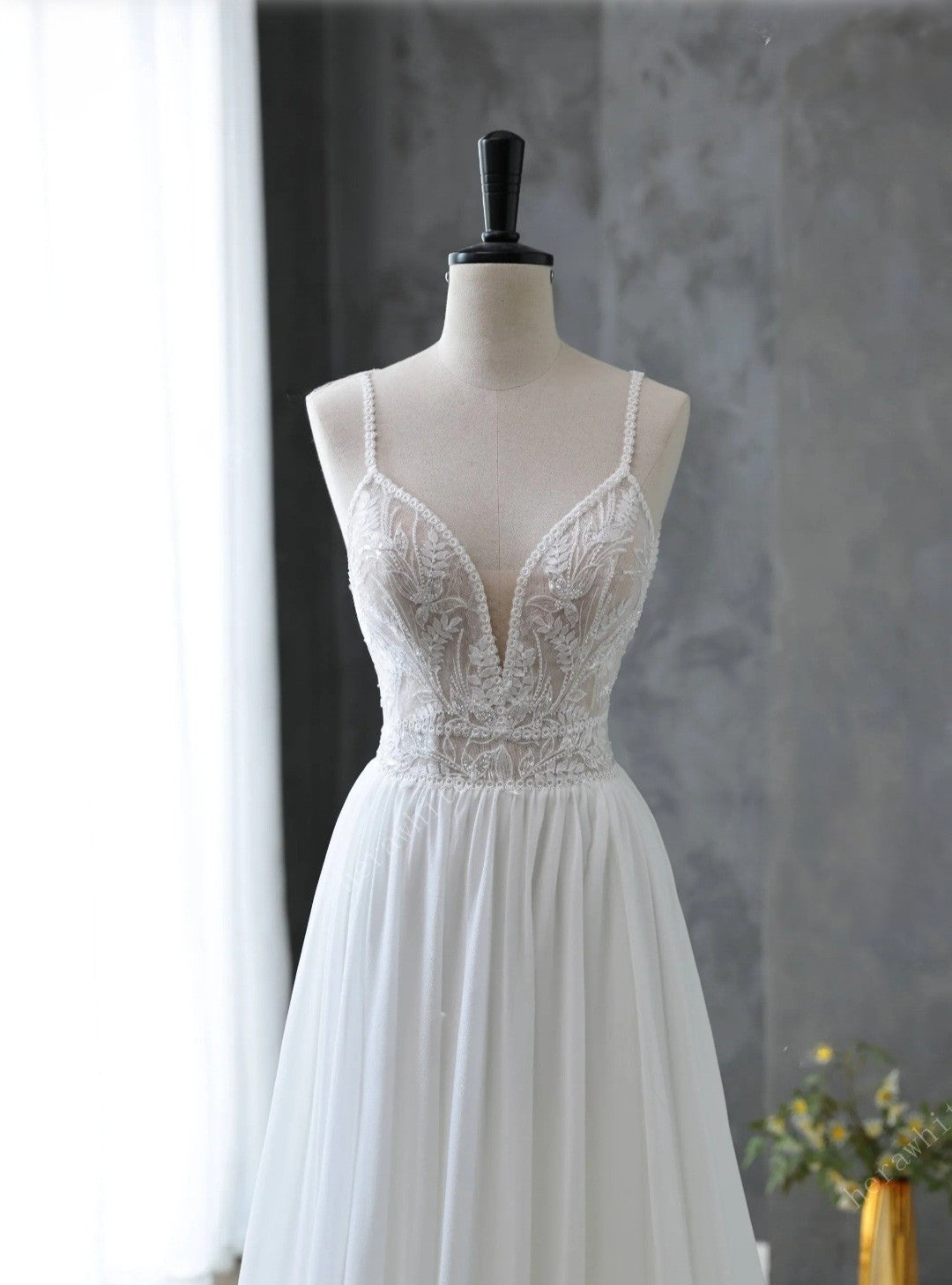 White lace dress on a mannequin against a gray wall with a vase of flowers.