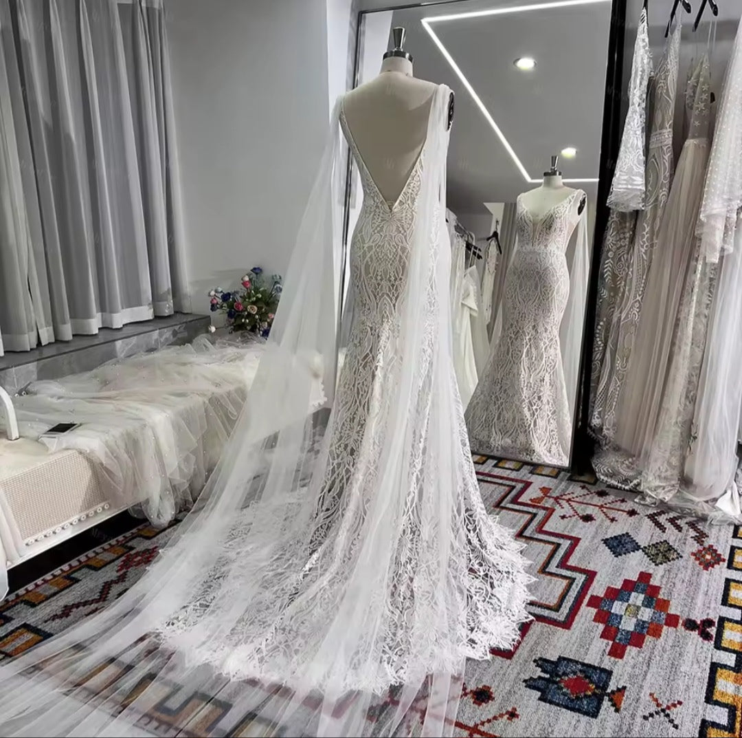 White lace wedding dress on a mannequin in a room with patterned rug and curtains.
