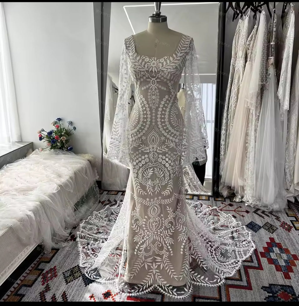 Elegant lace wedding dress on a mannequin in a room with floral decorations.