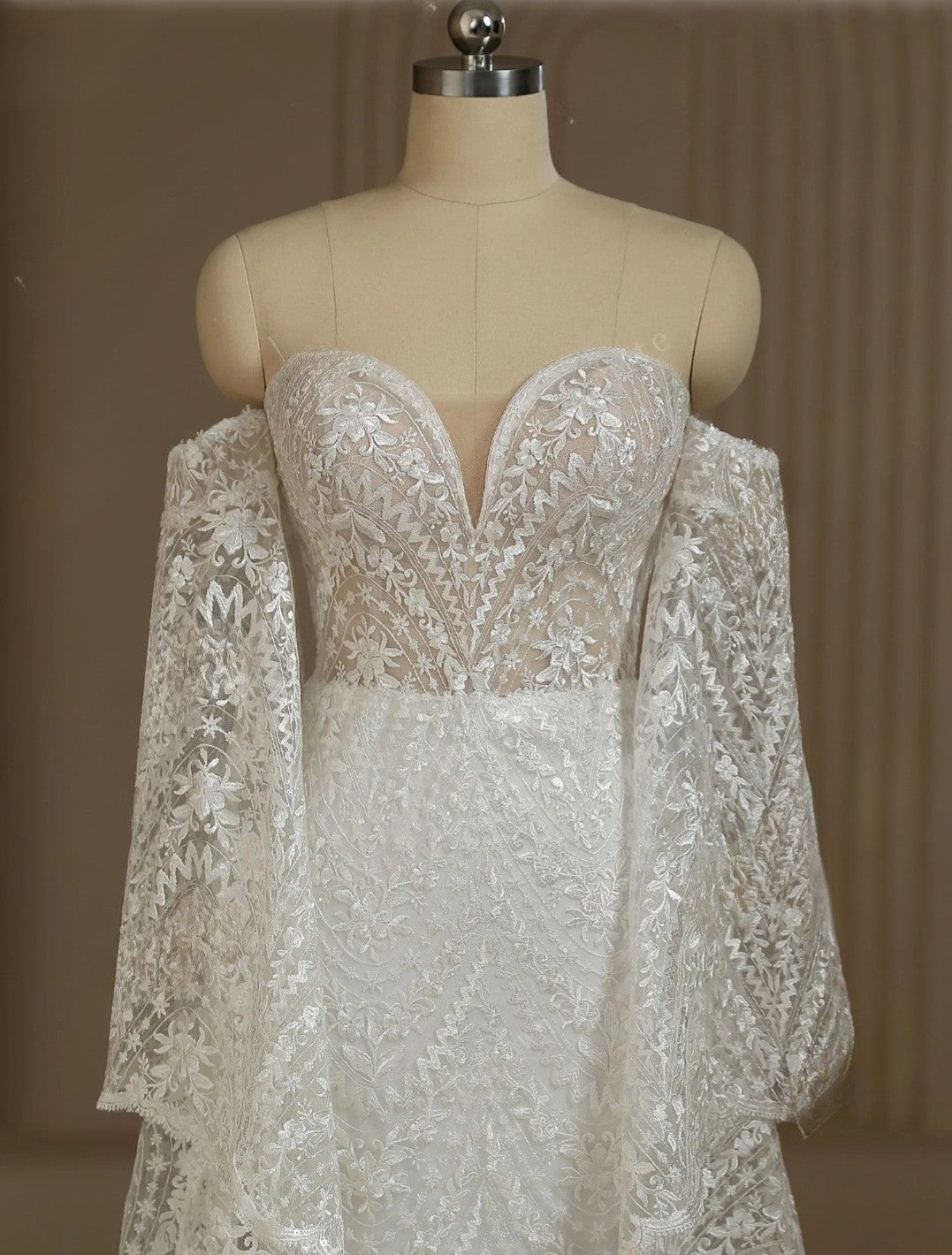 Lace wedding dress on a mannequin against a plain background