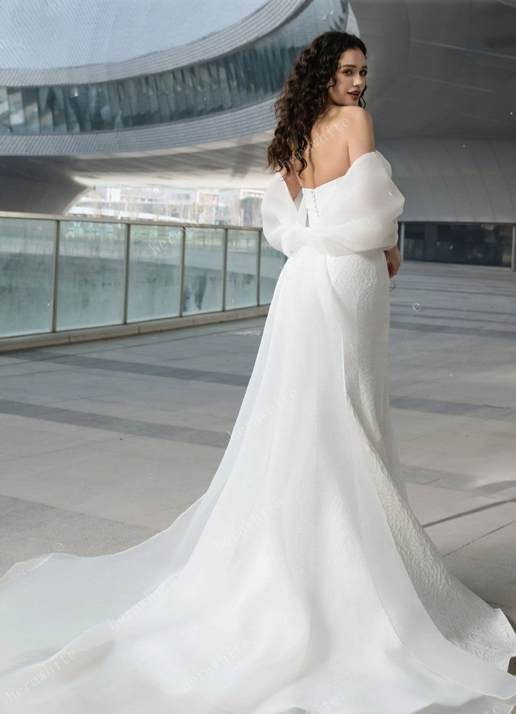 Woman in a white wedding dress with a flowing train in an indoor setting.
