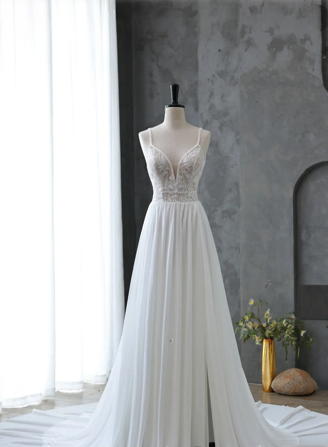 White wedding dress on a mannequin against a gray wall with a window in the background.