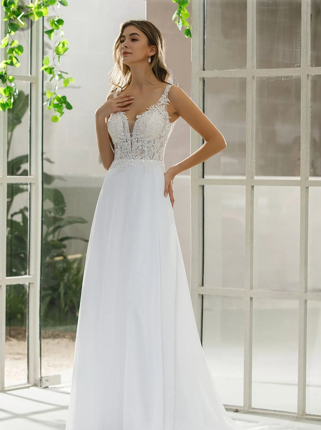 Woman wearing a white wedding dress with lace detailing in a bright room.