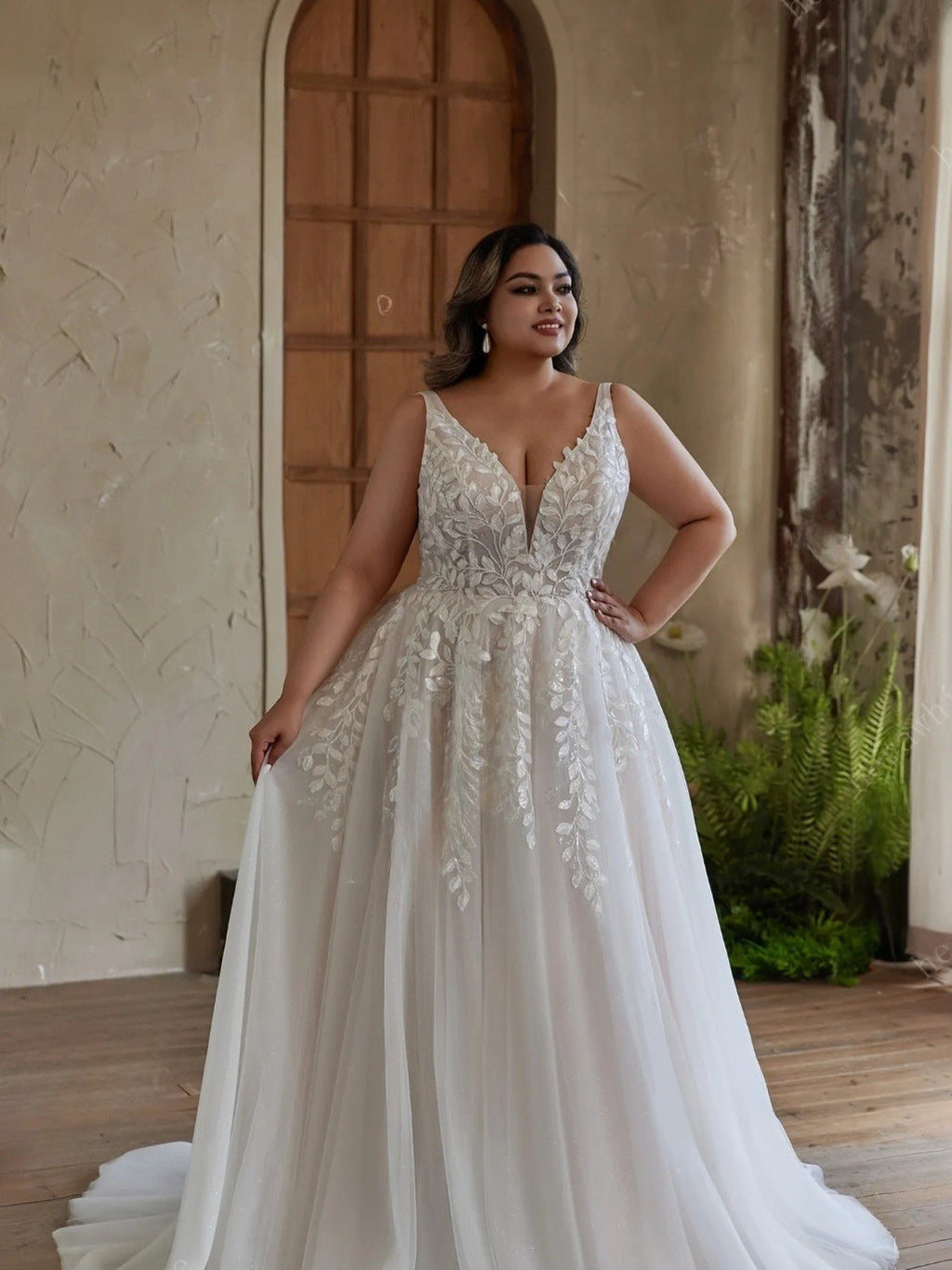 Woman in a white lace wedding dress standing in a rustic indoor setting.