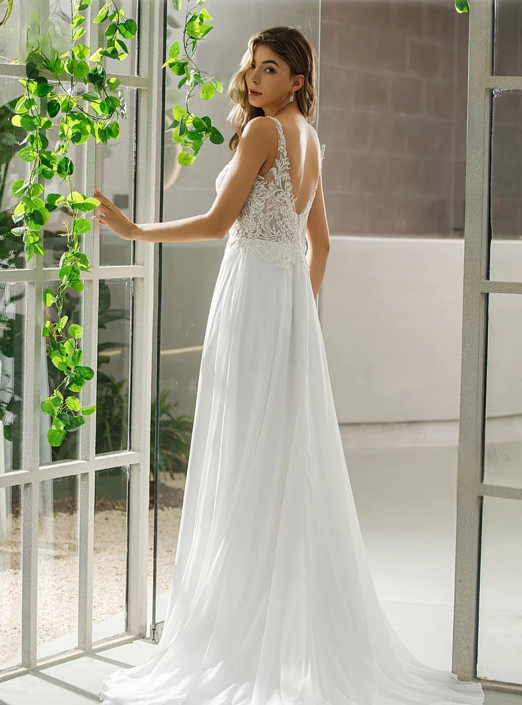 Woman in a white wedding dress standing indoors with greenery.