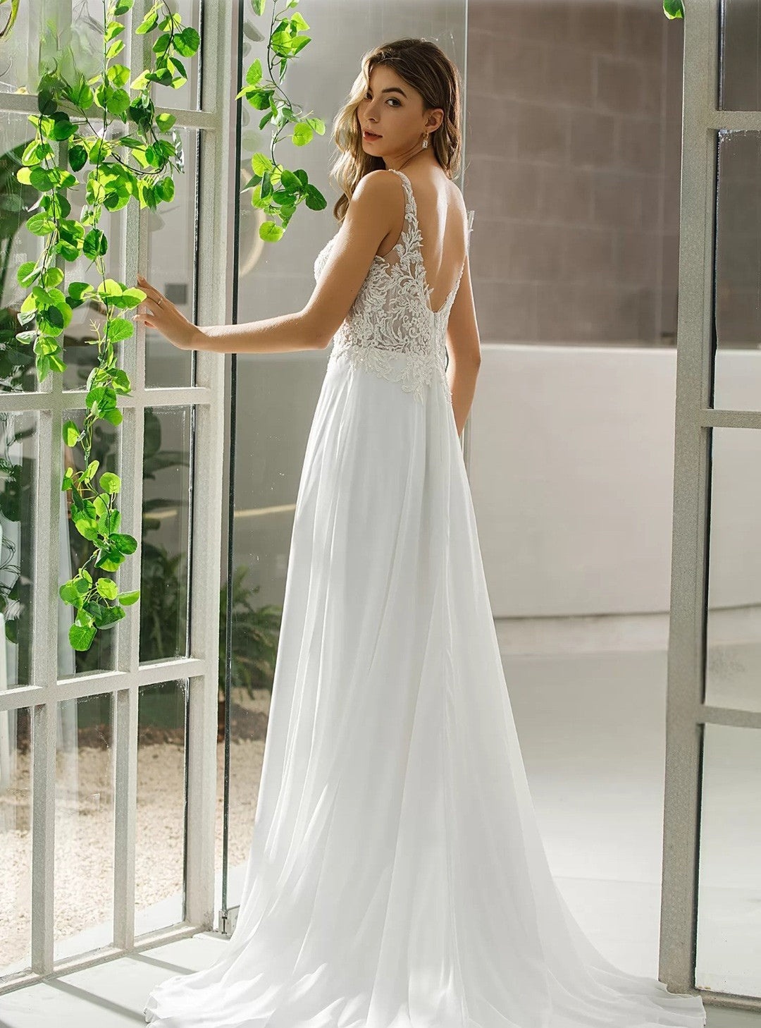 Woman in a white wedding dress standing indoors with greenery.