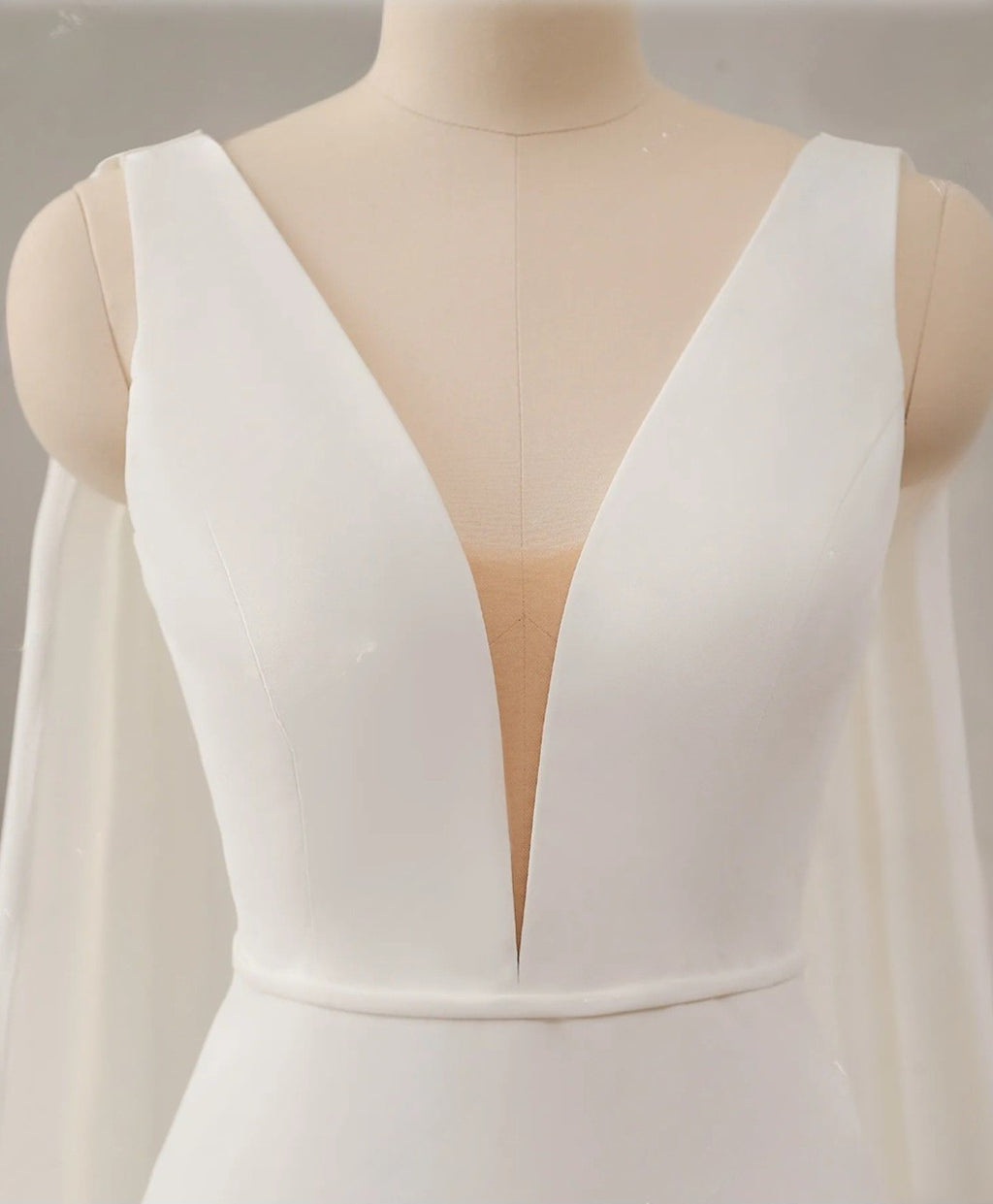 White dress with a deep neckline on a mannequin against a neutral background