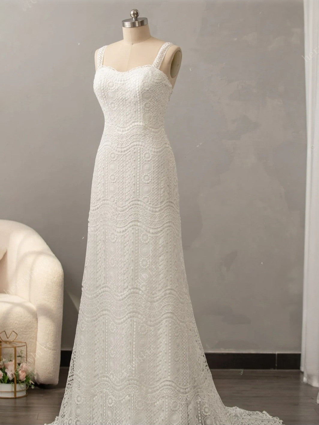 White lace wedding dress on a mannequin against a gray wall.