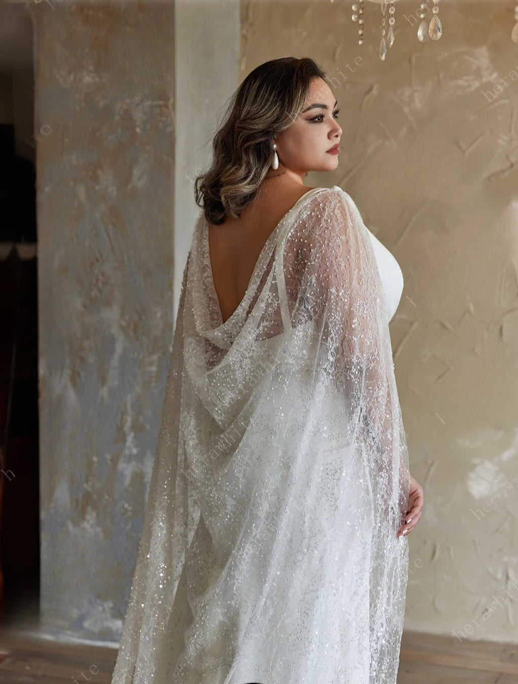 Woman wearing a sparkly, sheer wedding dress with a textured wall background