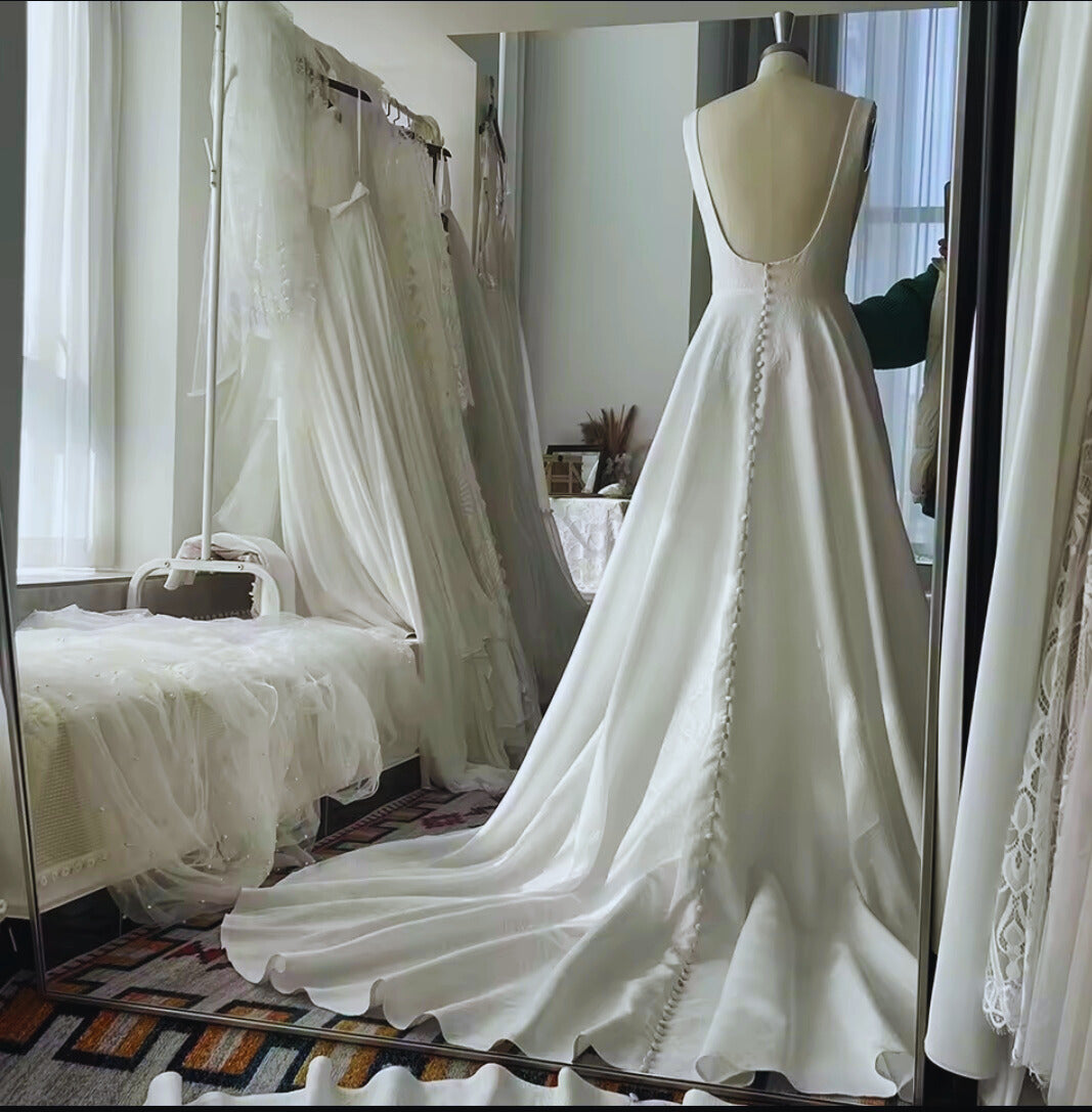 White wedding dress on a mannequin in a room with curtains and furniture.