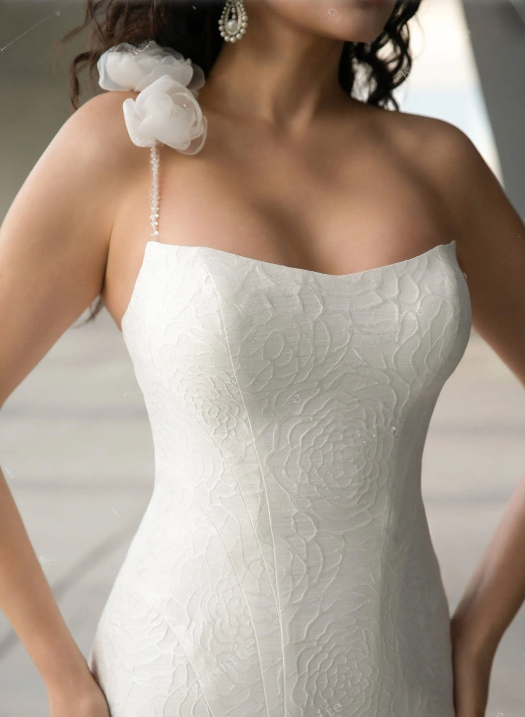 White strapless wedding dress with floral detail on shoulder against a neutral background