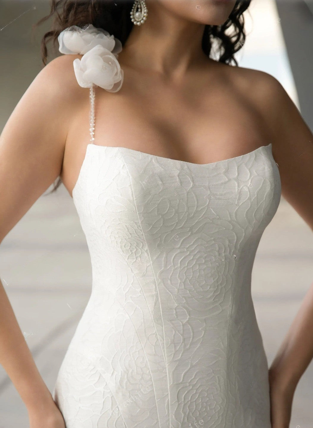 White strapless wedding dress with floral detail on shoulder against a neutral background
