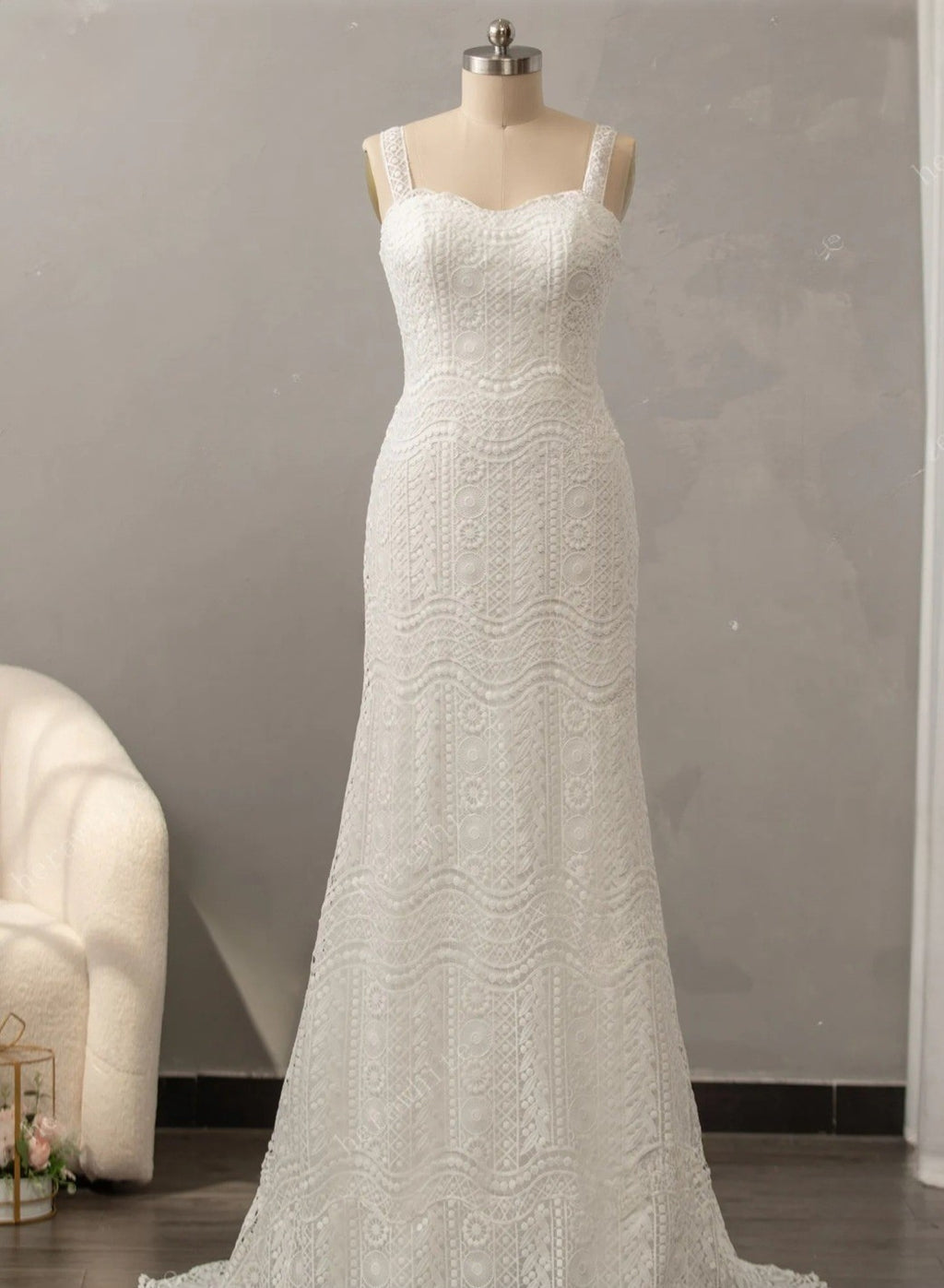 White lace wedding dress on a mannequin against a gray wall.