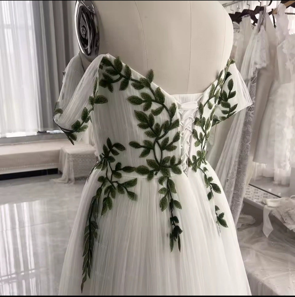 White dress with green leaf patterns on a mannequin in a store setting.