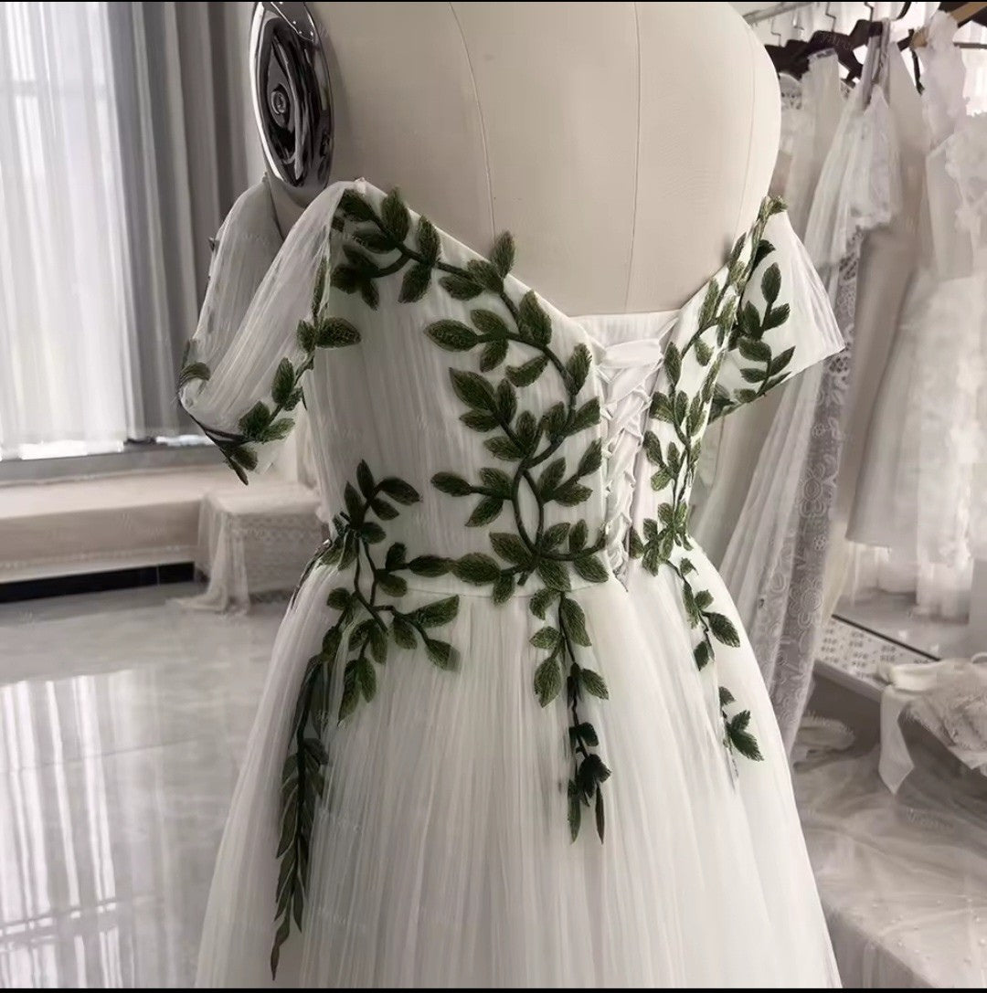 White dress with green leaf patterns on a mannequin in a store setting.