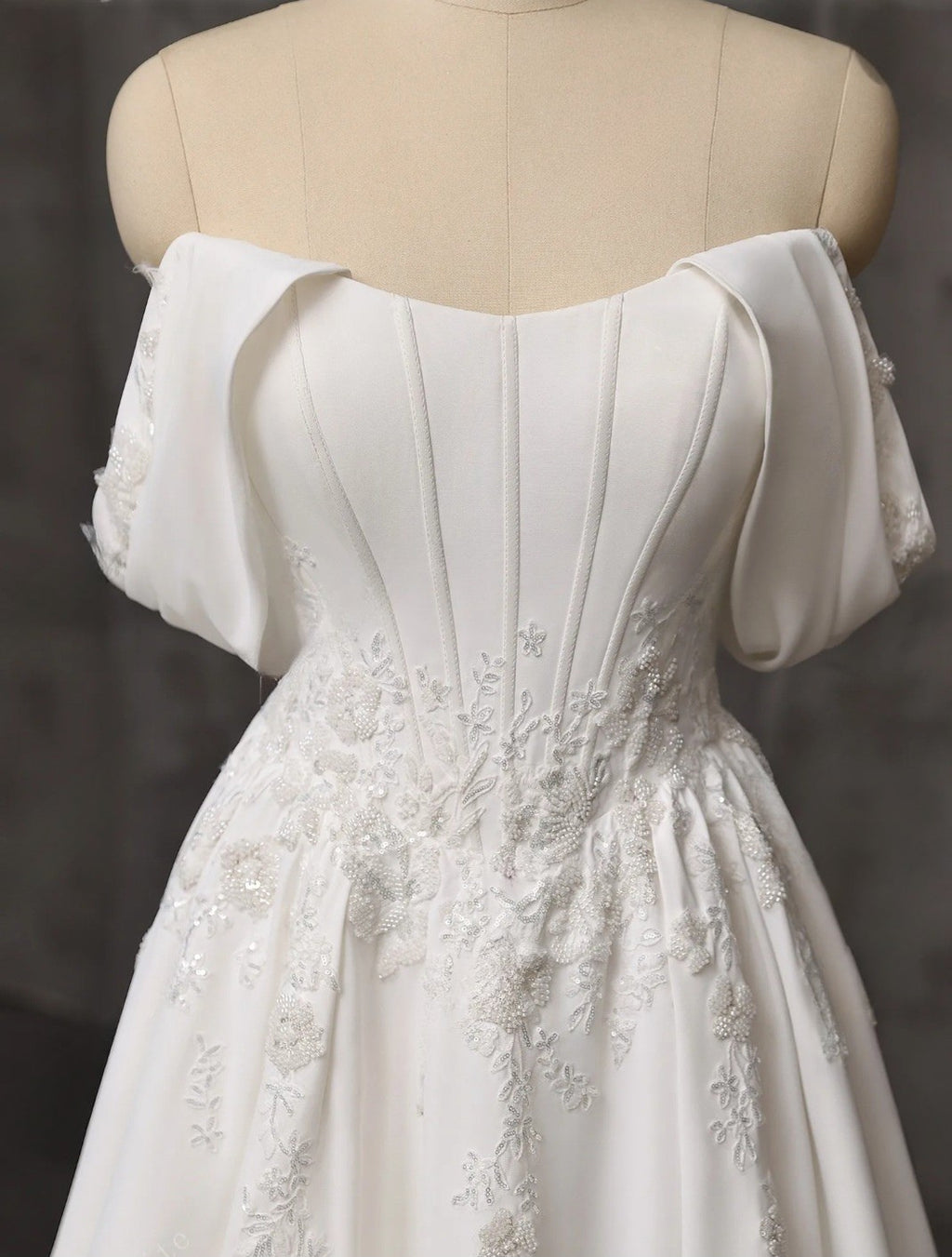 White off-shoulder dress with floral details on a mannequin against a dark background