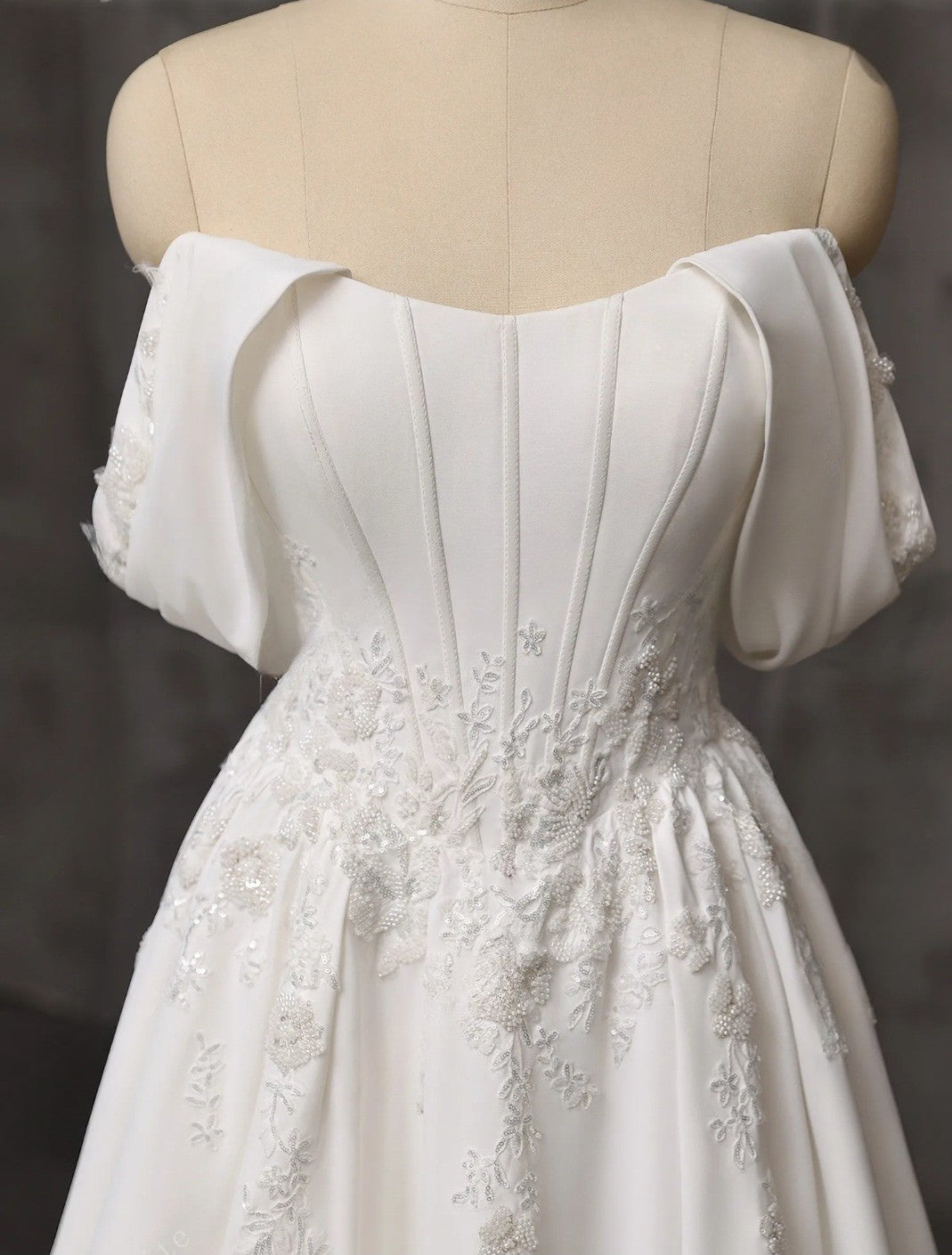 White off-shoulder dress with floral details on a mannequin against a dark background