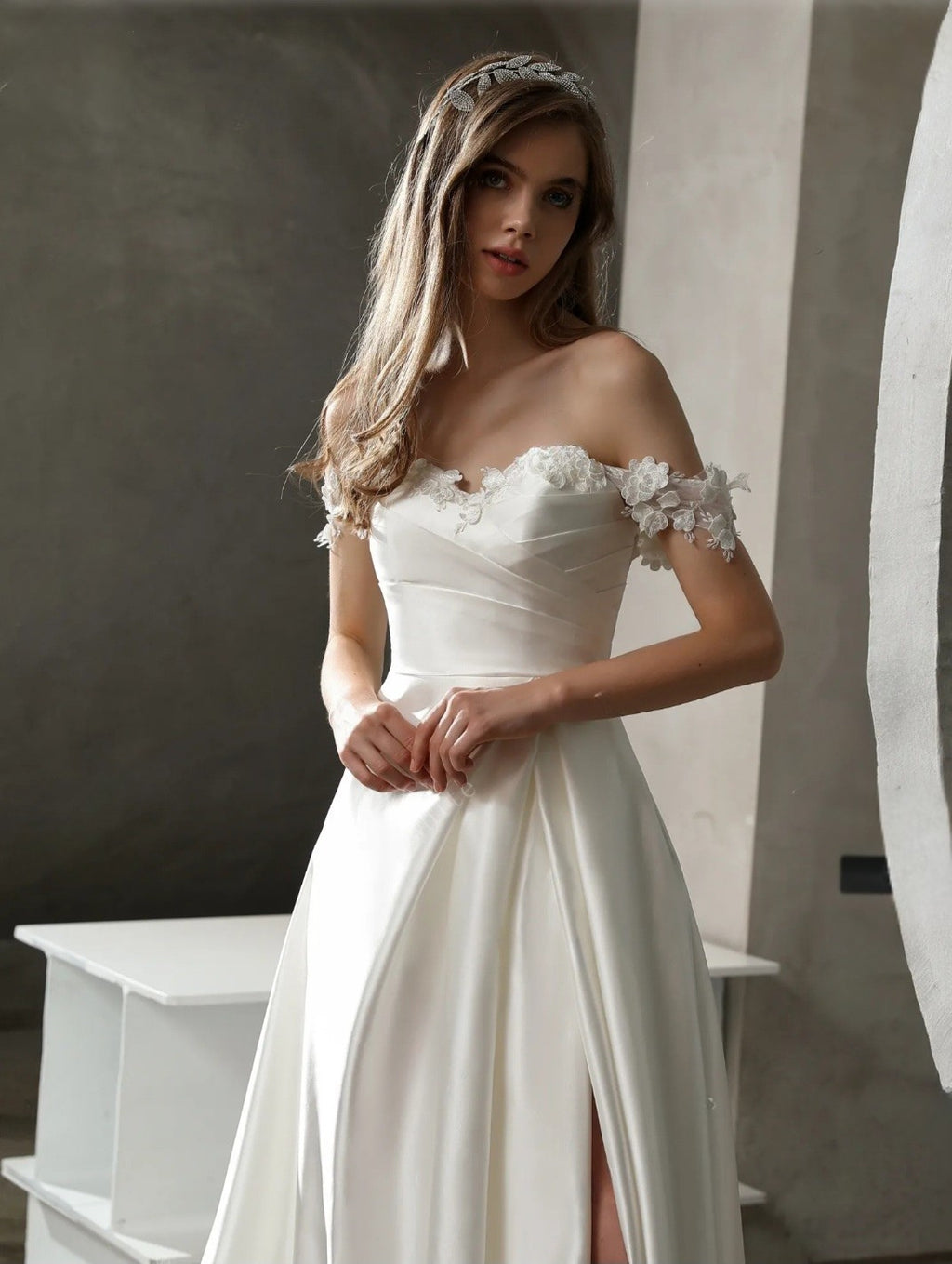Woman wearing a white wedding dress with floral details in a minimalistic setting.