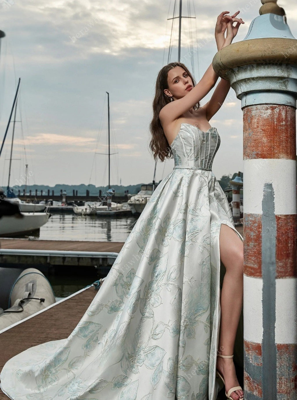 Woman in a strapless dress standing by a dock with boats in the background