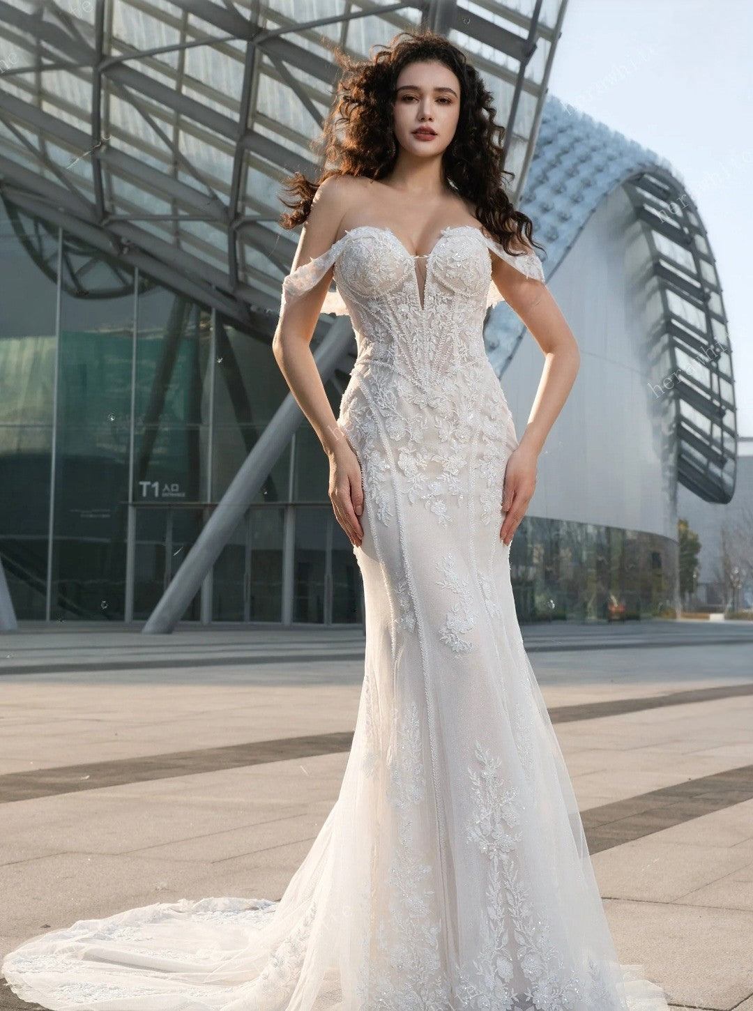 Woman in a white lace wedding dress standing in front of modern architectural structures.