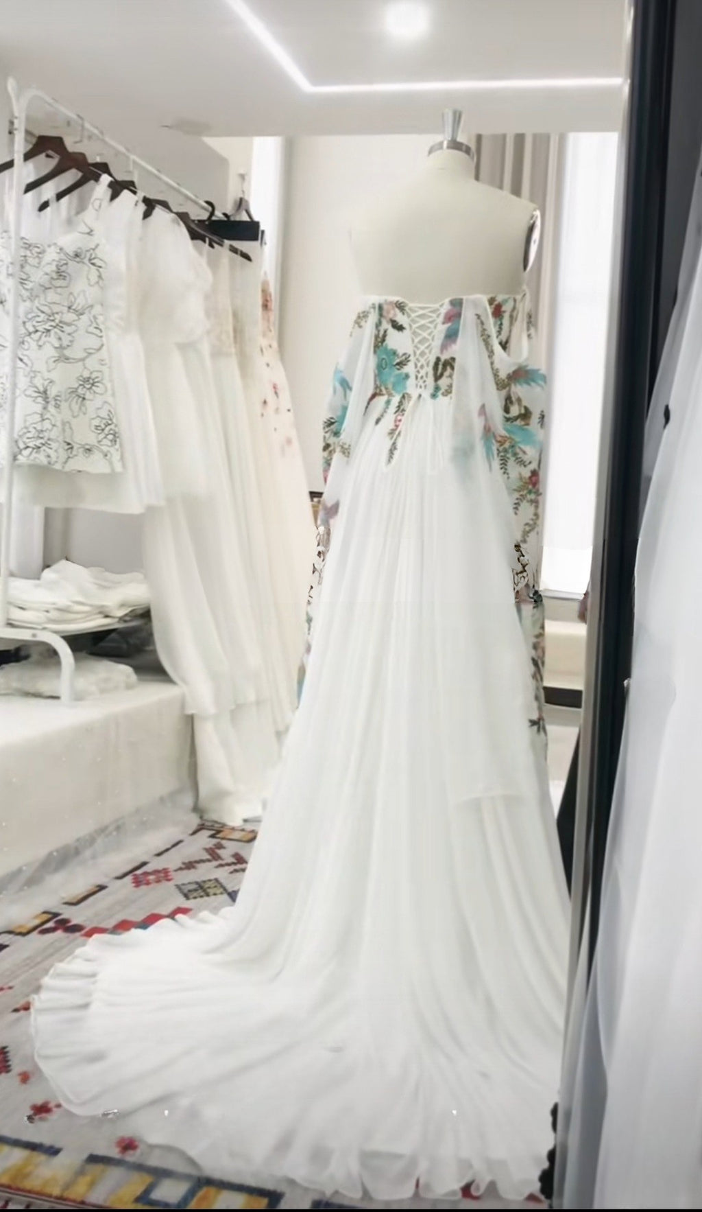 White wedding dress with floral details on a mannequin in a store setting.
