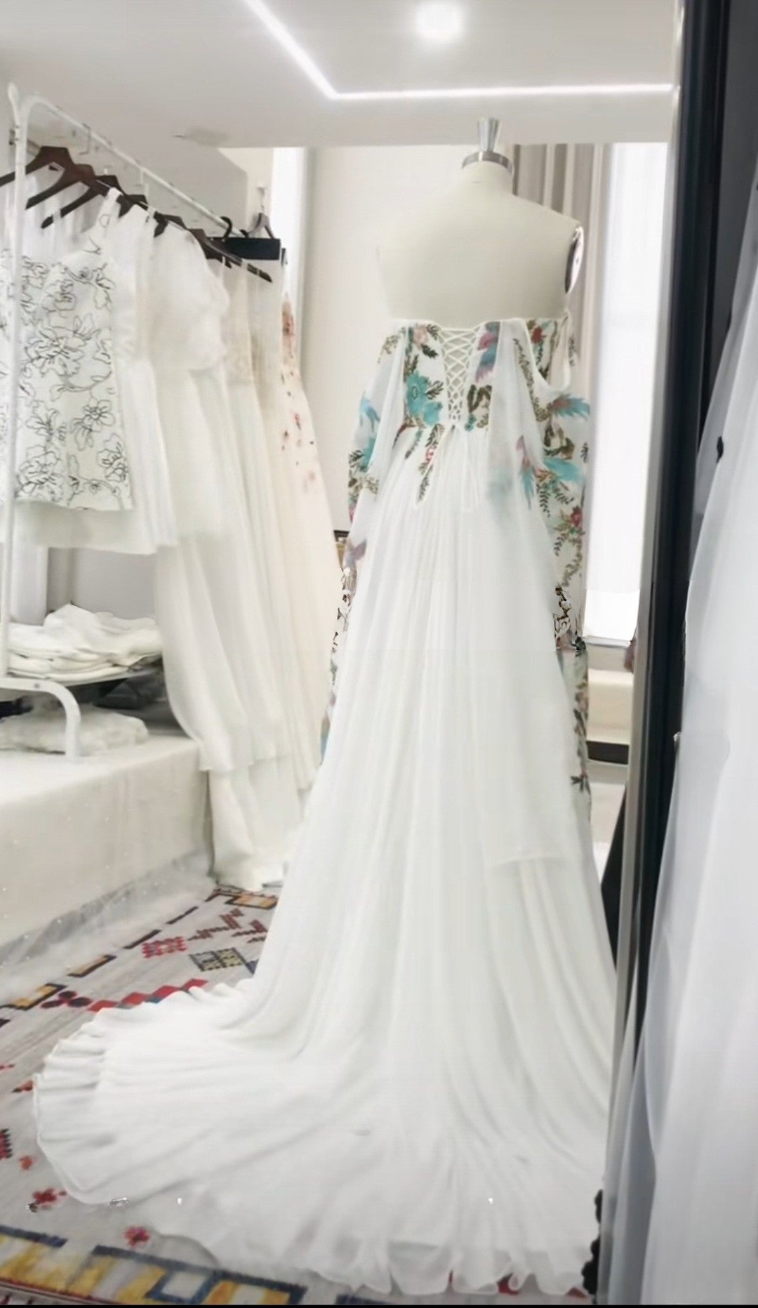 White wedding dress with floral details on a mannequin in a store setting.