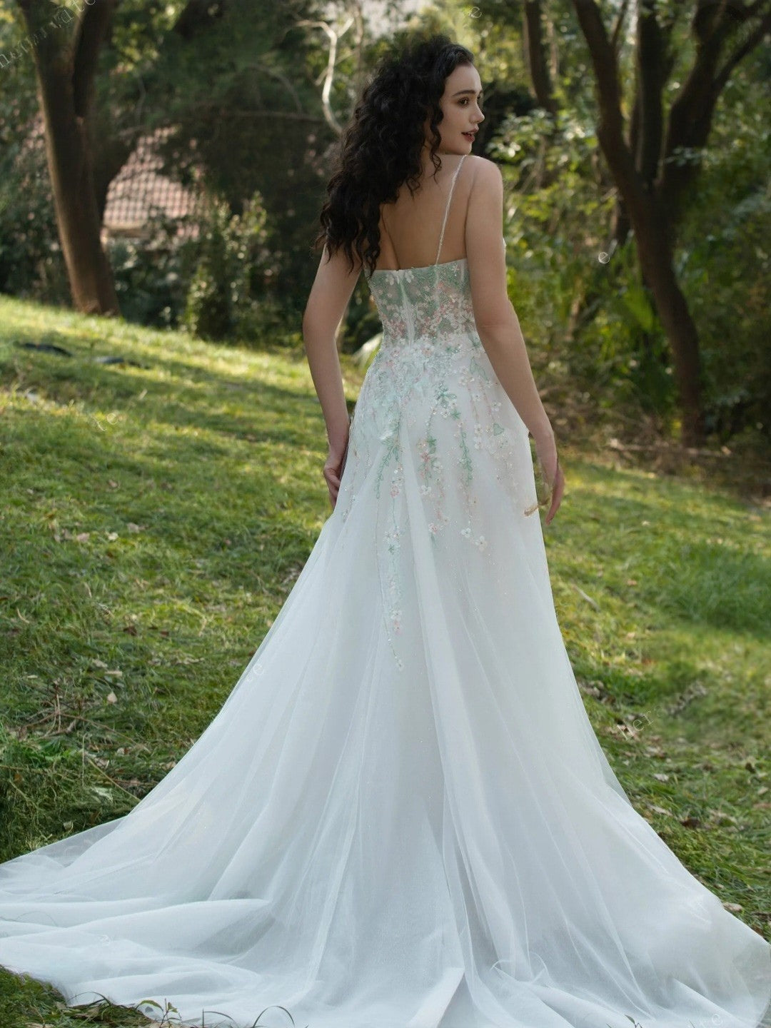 Woman in a white wedding dress standing in a grassy outdoor setting with trees.