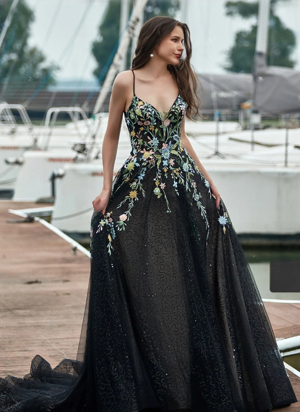 Woman in a black floral evening gown standing on a dock with boats in the background