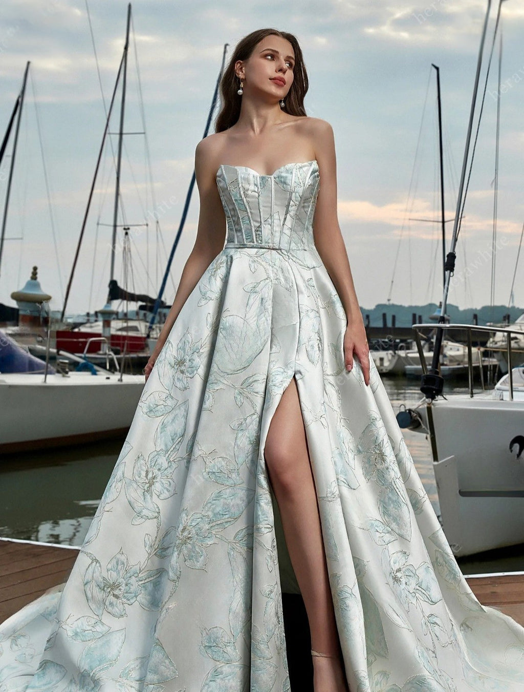 Woman in a strapless floral gown with a high slit standing by a marina.