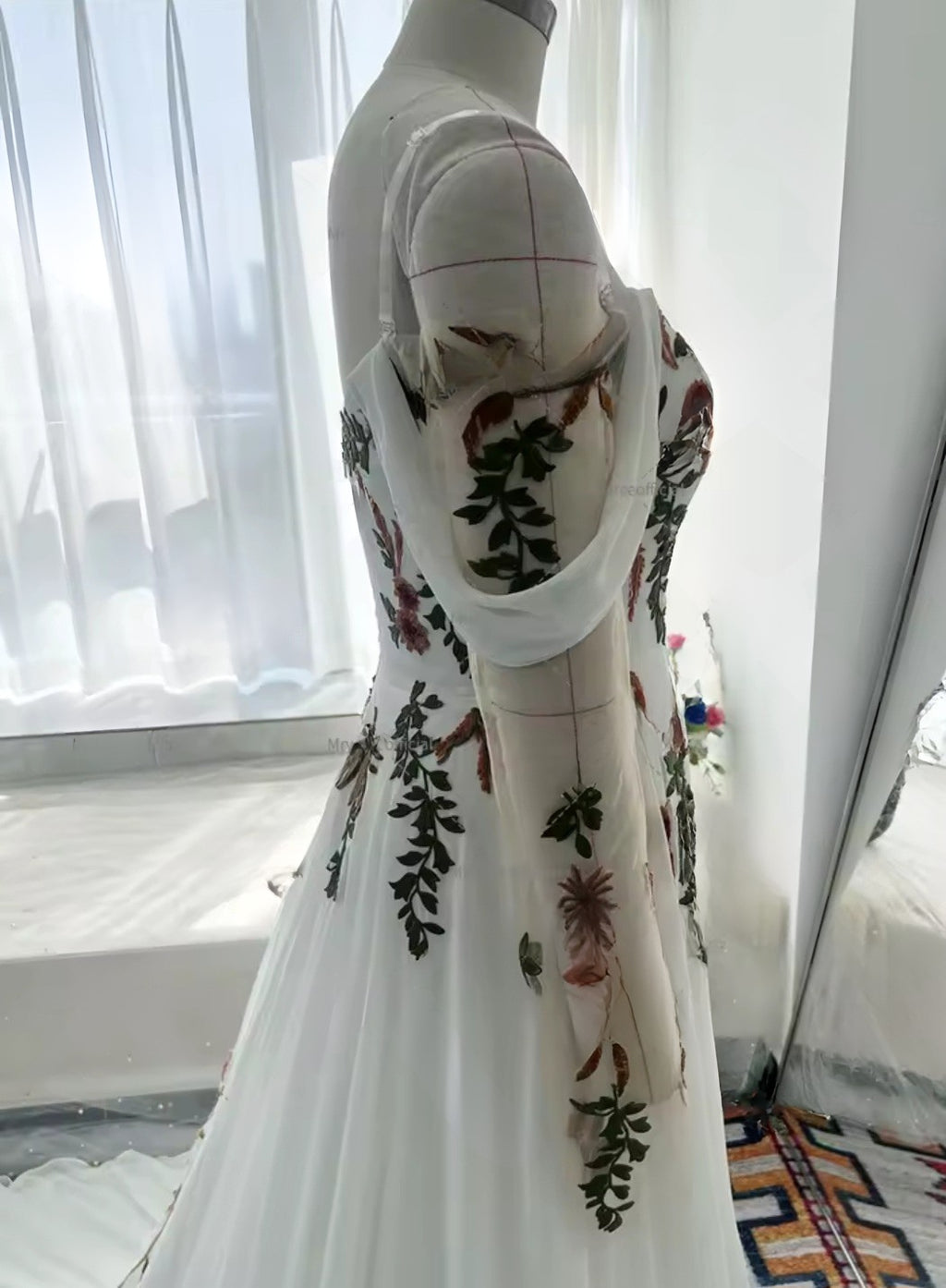 Mannequin wearing a white dress with floral embroidery in a room with a window.