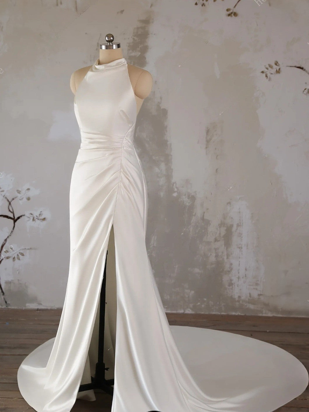 White evening gown on a mannequin against a textured wall.
