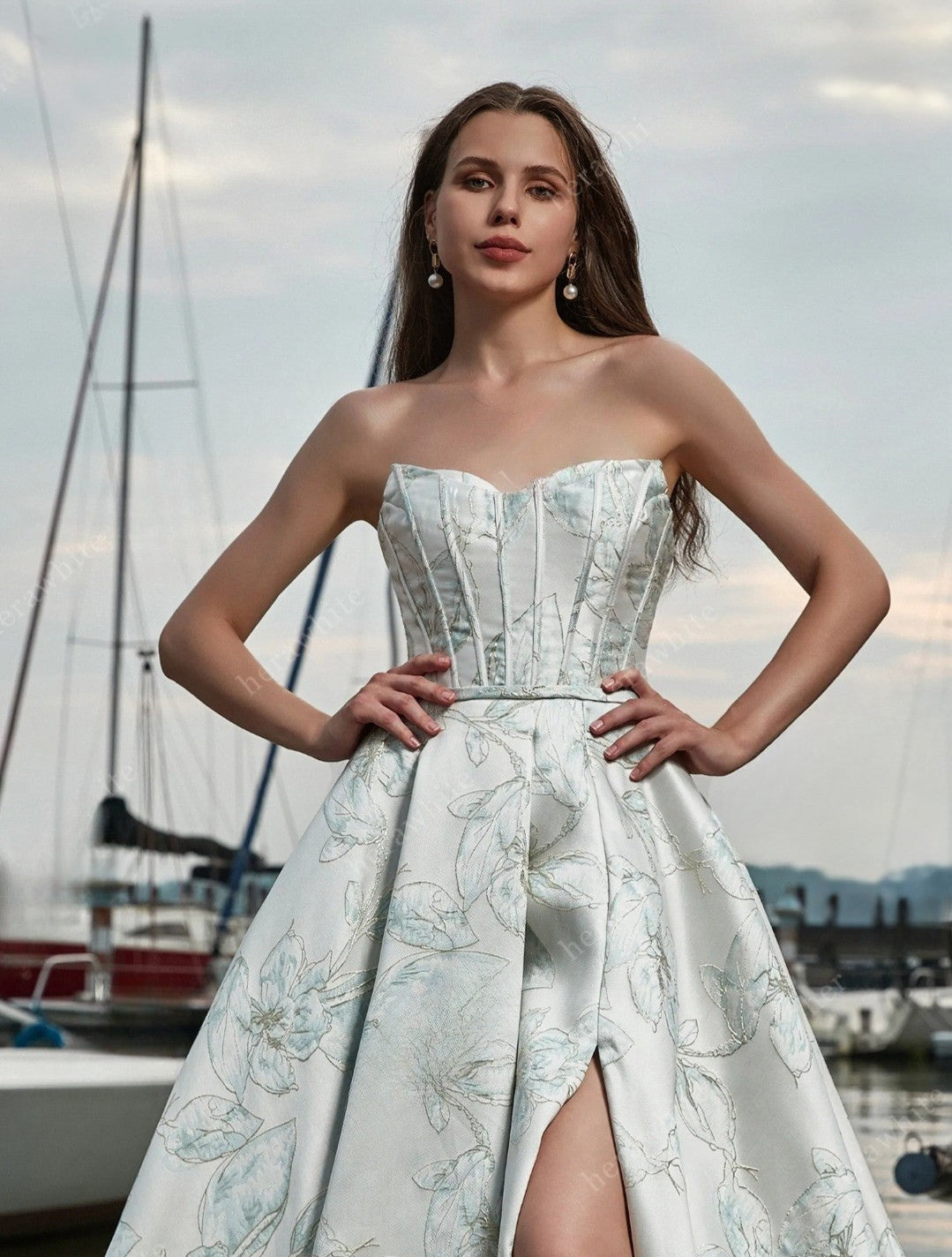 Woman in a strapless floral dress standing by a marina with boats in the background