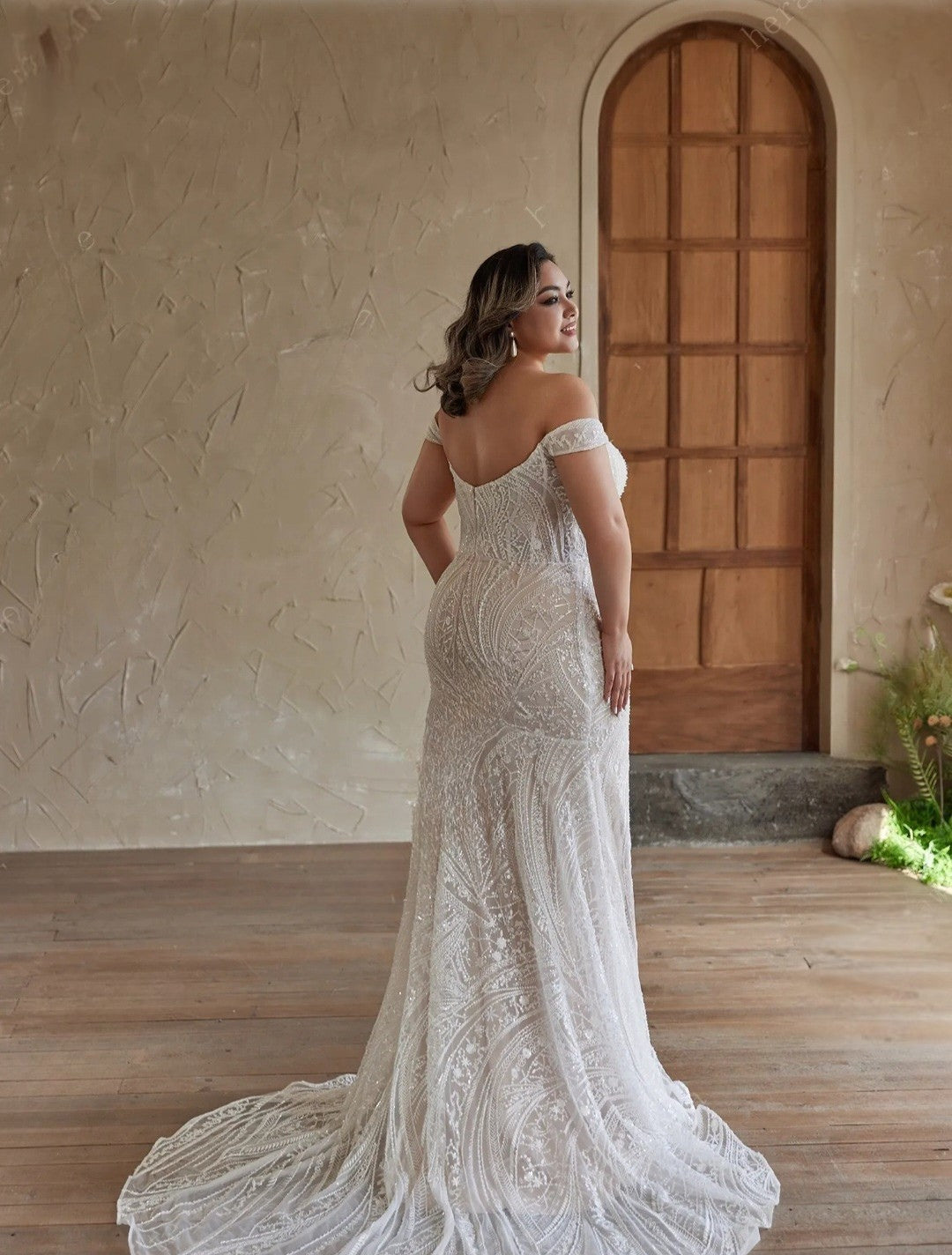 Woman in a white lace wedding dress standing in a rustic indoor setting.