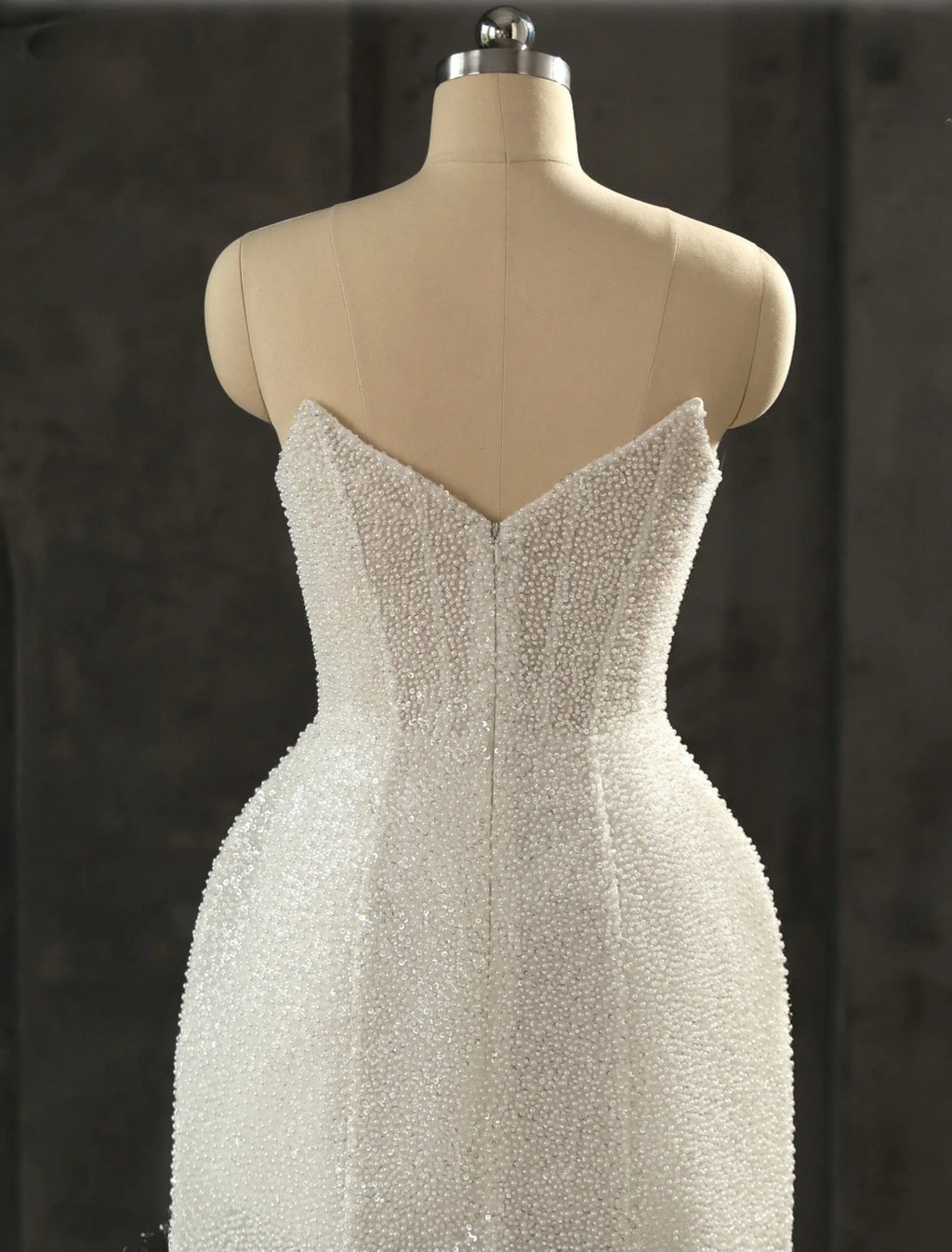 Beaded white evening gown on a mannequin against a dark background