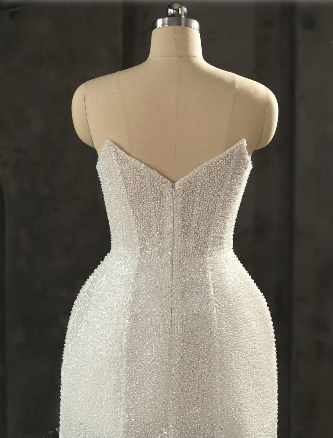 Beaded white evening gown on a mannequin against a dark background