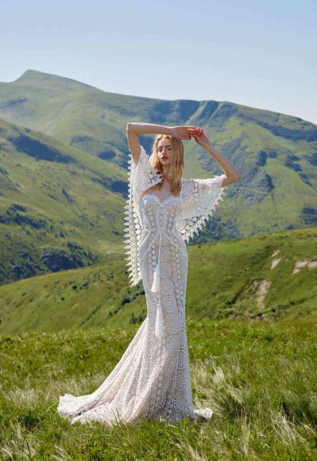 Woman in a white lace dress standing in a mountainous landscape