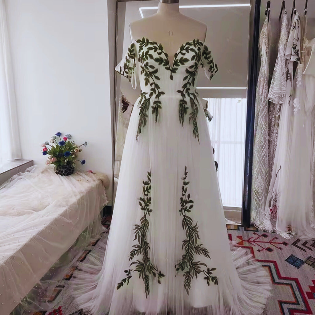 White evening gown with green leaf patterns on a mannequin in a room.