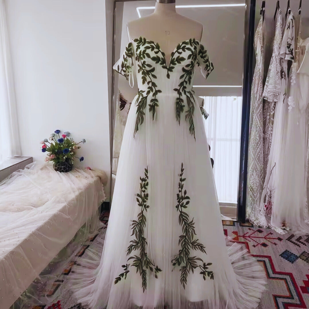 White evening gown with green leaf patterns on a mannequin in a room.