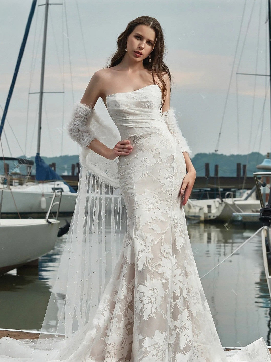 Woman in a white lace wedding dress standing by a marina with boats in the background