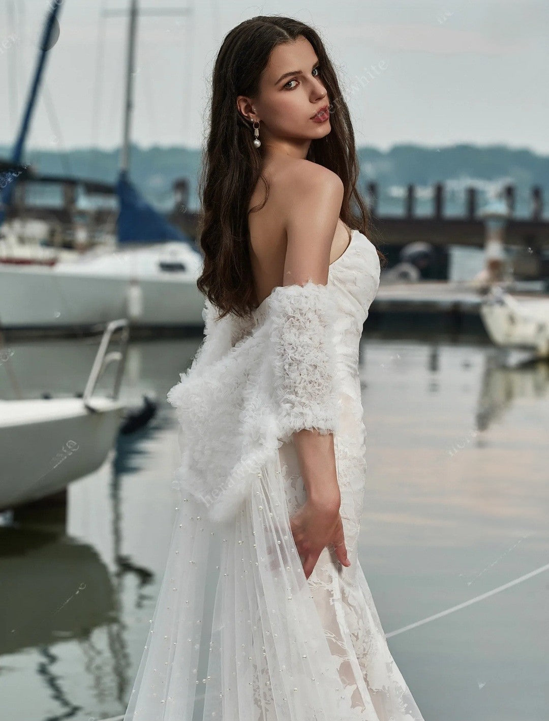 Woman in a white dress standing by a marina with boats in the background