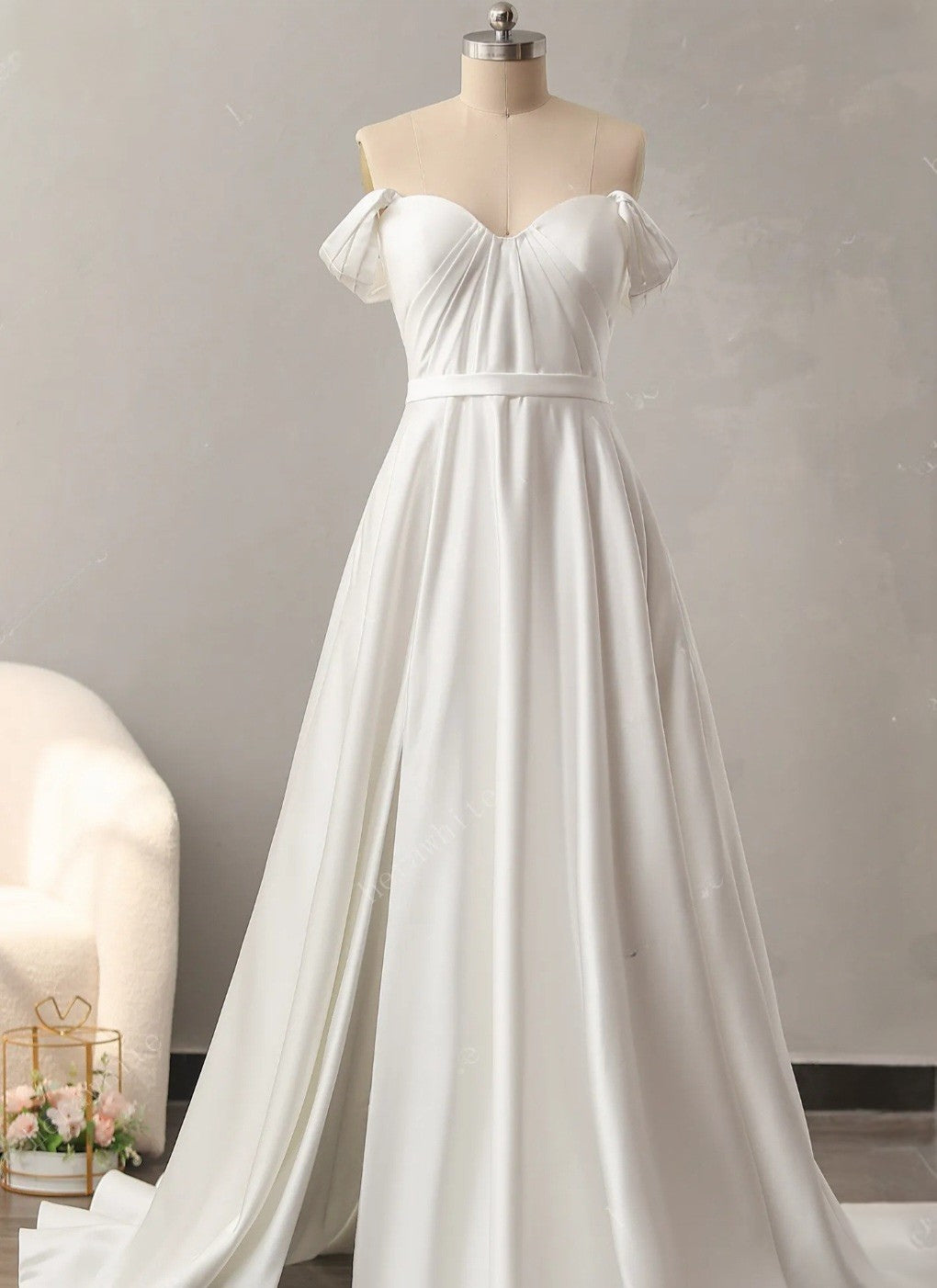 White off-shoulder wedding dress on a mannequin against a plain background