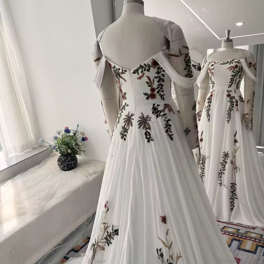 White dress with floral embroidery on a mannequin in a room with a window and flowers.